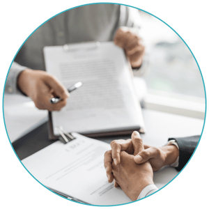 A pair of hands holds up a clipboard with illegible text and points to something. Another pair of hands is folded, like they are listening attentively.